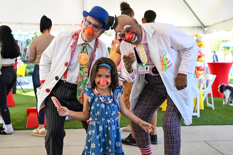 Two red nose clown doctors with young girl.