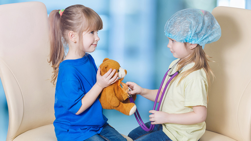 two girls playing doctor with a teddy bear