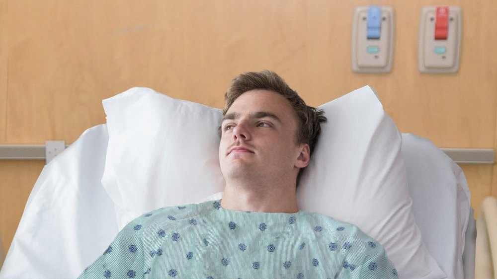 young man looking pensive while laying on hospital bed.