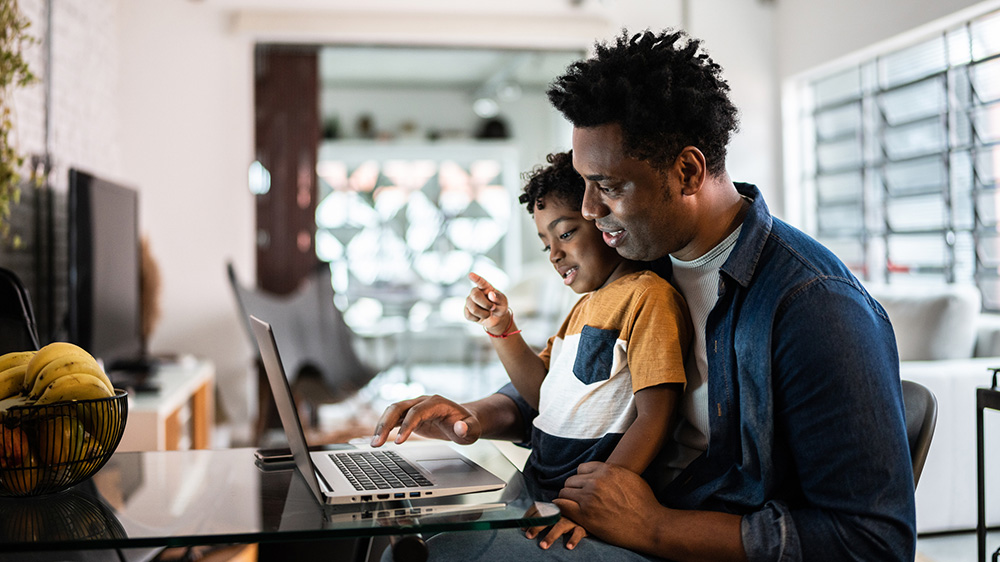 father and son looking at laptop from kitchen table.