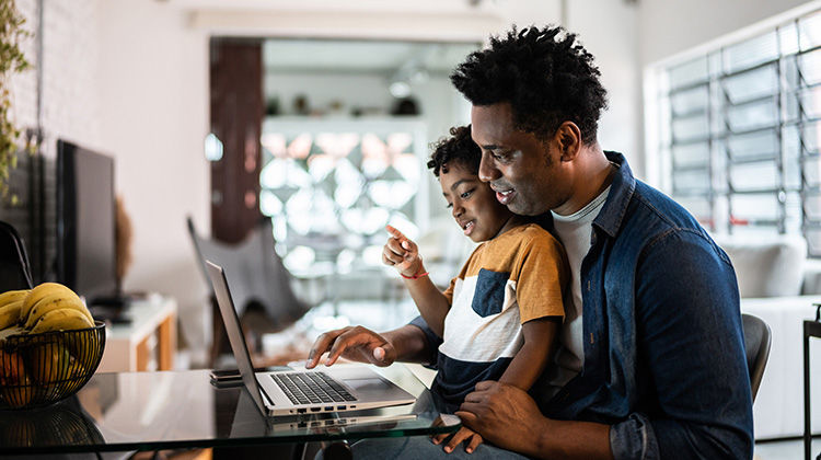 padre e hijo mirando una computadora portátil desde la mesa de la cocina.