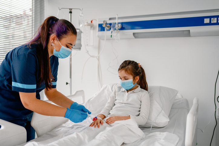 nurse with ponytail and facemask checking girl's IV.