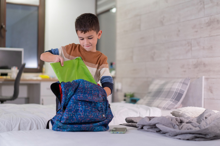 boy packing items into his backpack.