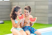 Brother and sister eating watermelon by the pool
